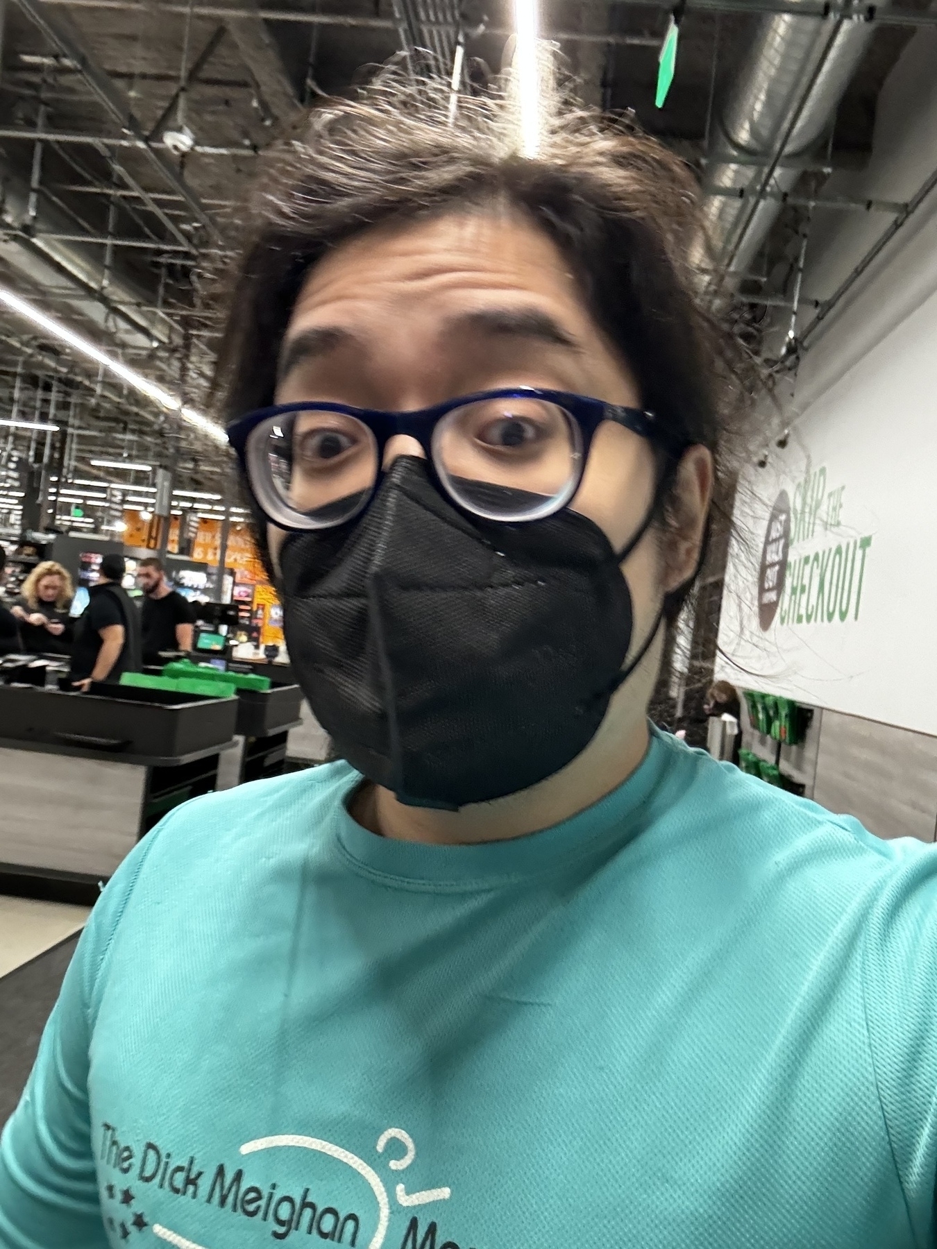 Miguel a masc Filipino man with black hair and a black mask inside an Amazon fresh grocery store. Wearing a teal long sleeve shirt. 