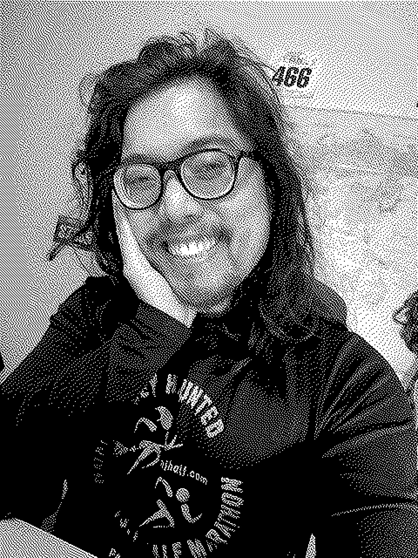 Black and white 1-bit retro-style selfie via BitCam of Miguel a masc Filipino man. He is smiling and seen from chest up. His right hand is resting on his face. His head is tilted slightly to his right side. He is wearing a black long sleeve. A map is on the wall behind him. 