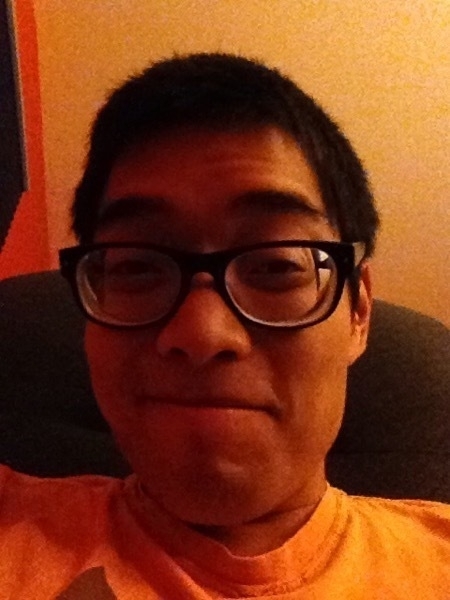selfie of miguel a masc filipino man with short hair and glasses in a room with orange walls
