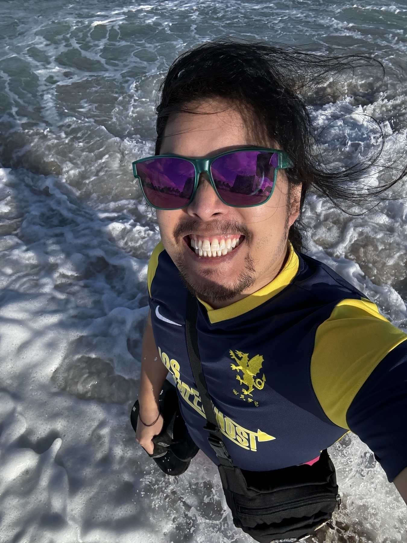 Miguel a masc Filipino man standing in the Atlantic ocean in the daytime wearing sunglasses 