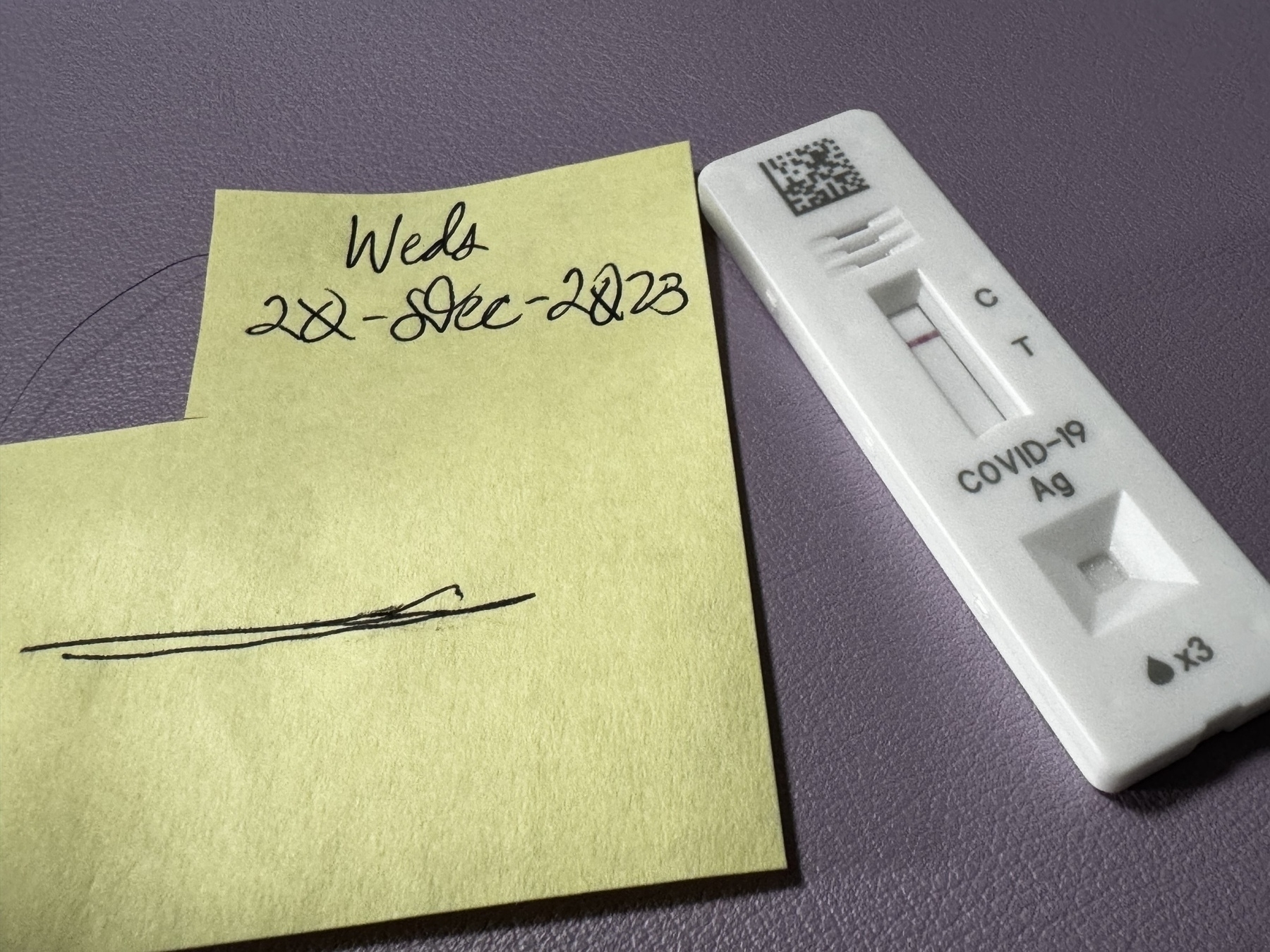 A negative COVID-19 rapid antigen test next to a sticky note with handwritten text.