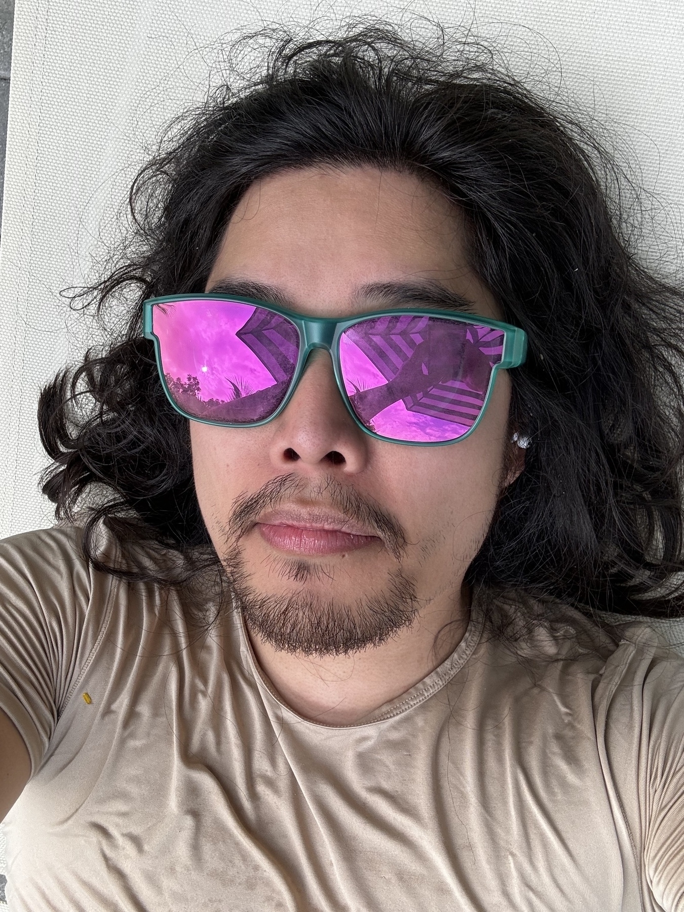 Miguel a masc Filipino man with black hair is looking at the camera with teal sunglasses with mirrored lenses. Not smiling