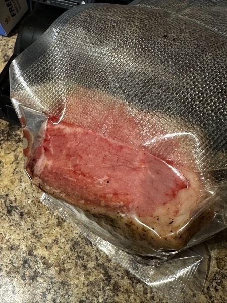 rare steak on a kitchen counter top. it is vacuum sealed in a bag. it is very rare. it is oval shaped.