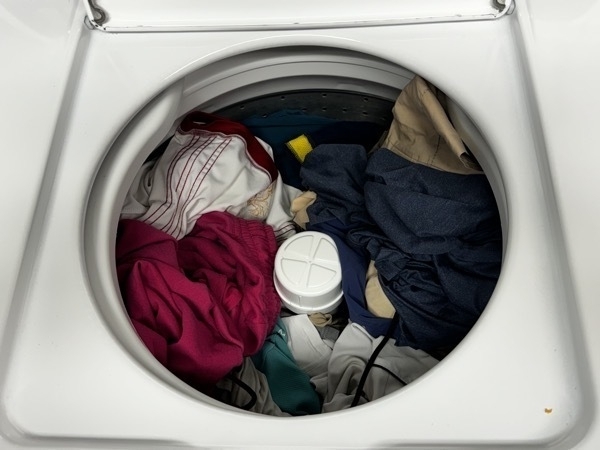 a top loading washing machine with the lid open and various clothes inside. whites and colours are mixed because....