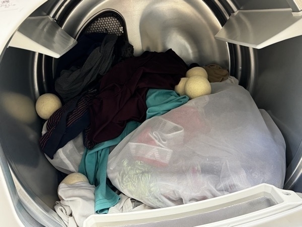 the inside of a dryer machines. a bag full of underwear is near the front. shirts are tossed about. there are wool balls inside.