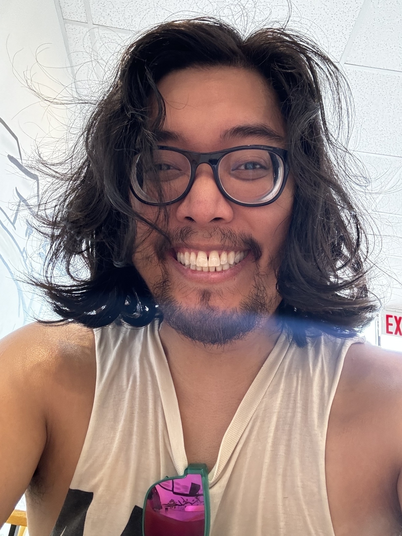 A person with long dark hair, glasses, and a big smile wearing a sleeveless shirt.