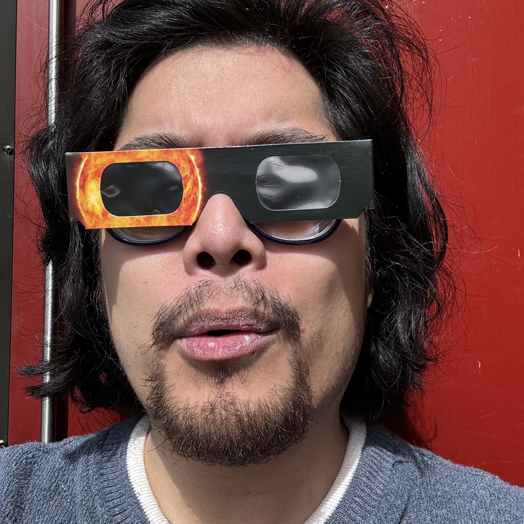  A selfie of a person wearing paper eclipse glasses with an image of the sun printed on them.