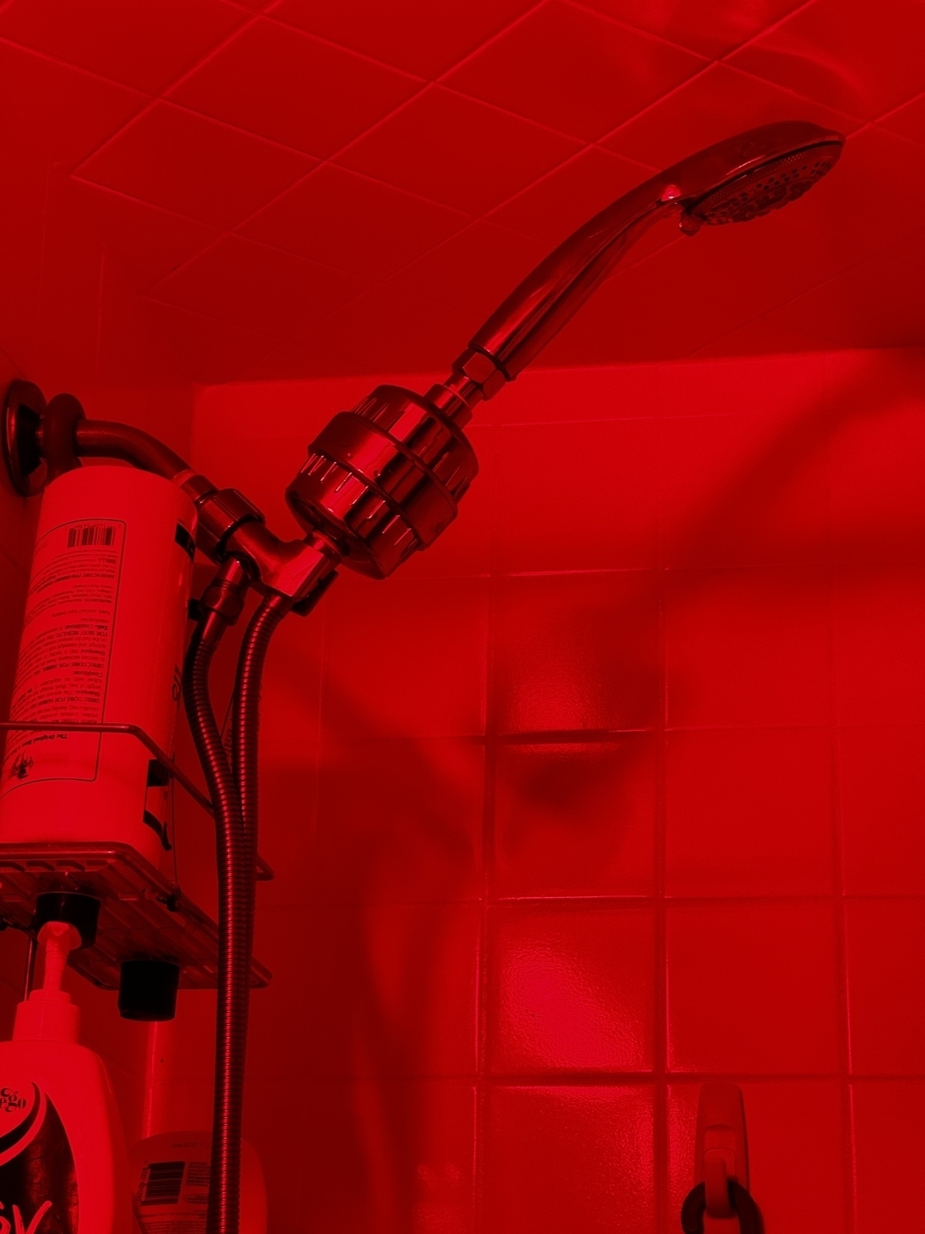  A shower head and water filter in a red lit shower.