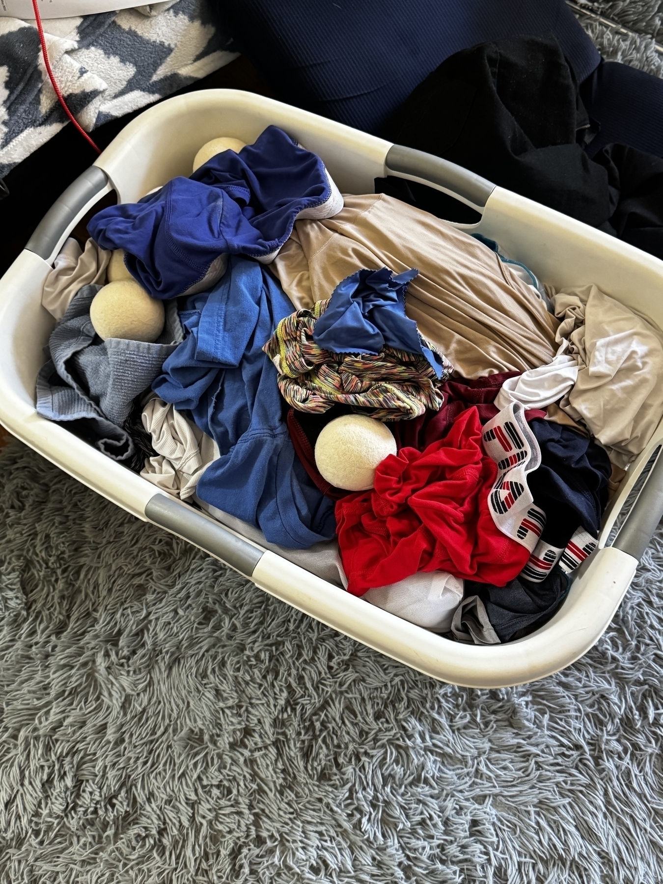  A white plastic laundry basket full of clothes and 3 dryer balls.