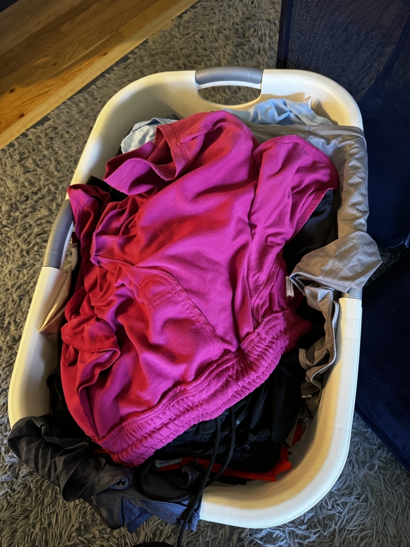  A laundry basket full of clothes, including a bright pink pair of shorts.