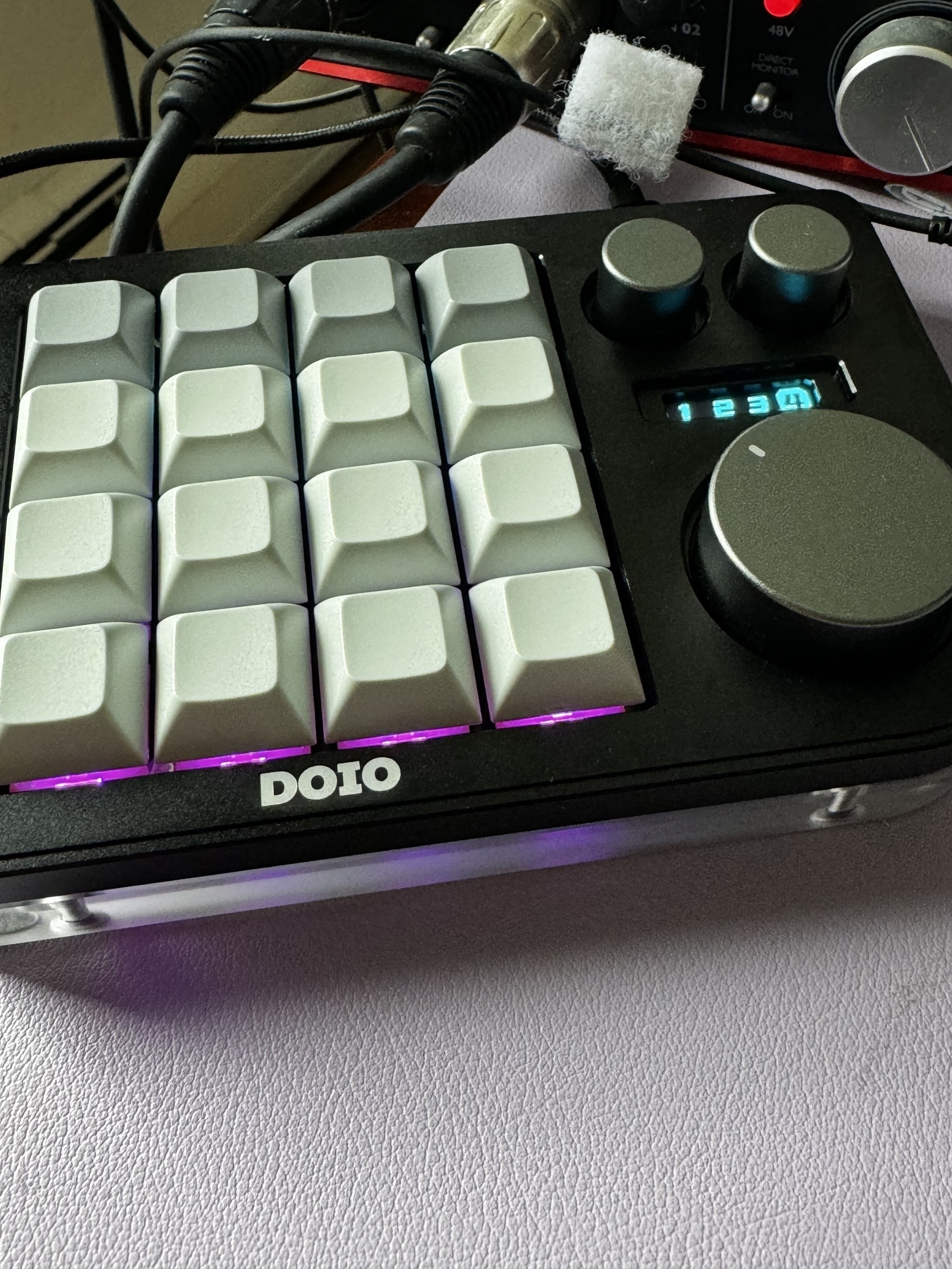 A black and white mini macro pad with 16 backlit keys, 3 knobs, and a small screen.