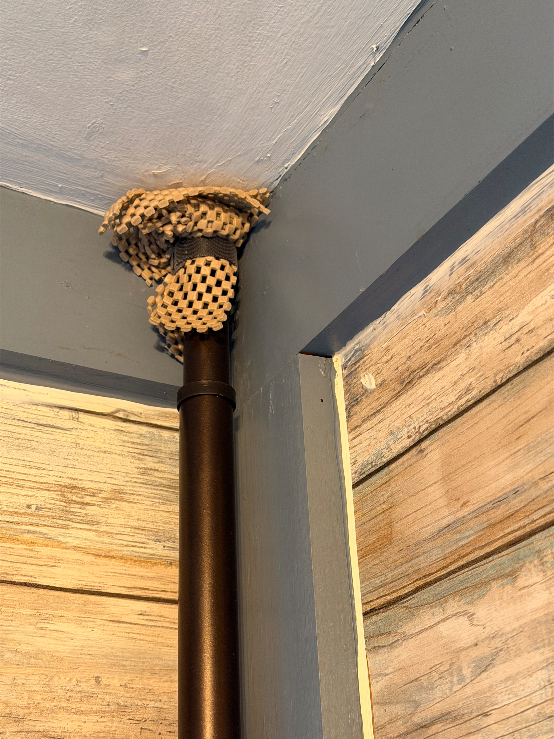 Shelf liner around a pipe or rod in the corner of a shower with wooden paneling.