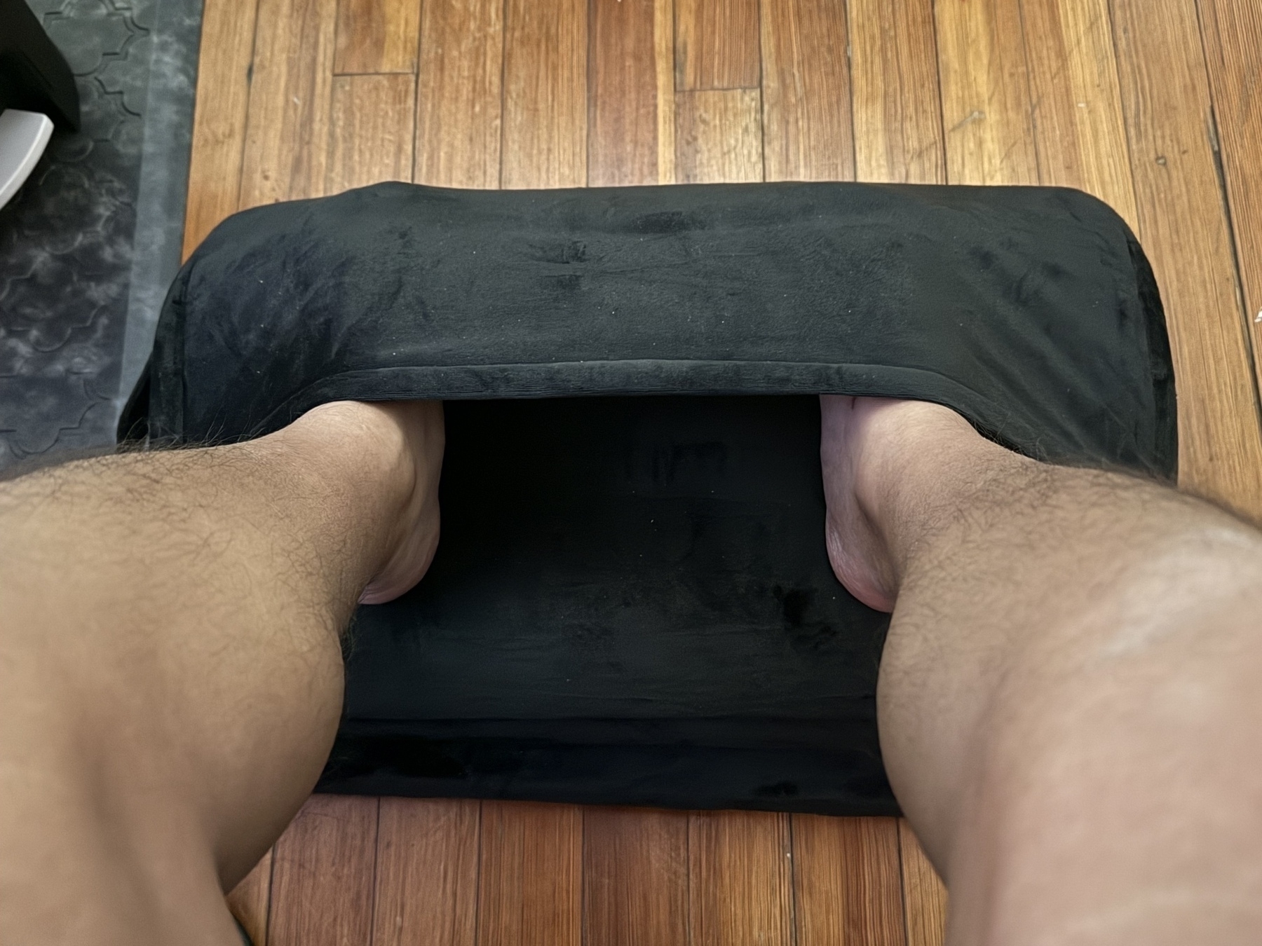 A person is using a cushioned foot rest with pockets for feet on a wooden floor.